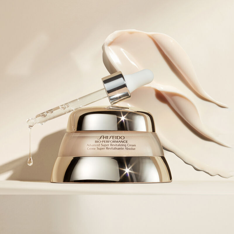 " The Shiseido Bio-Performance Advanced Super Revitalizing Cream with a dropped tool emitting a clear, bubble-like texture. There is a swatch of the product beyond the jar itself, all resting against a beige-colored background.  "