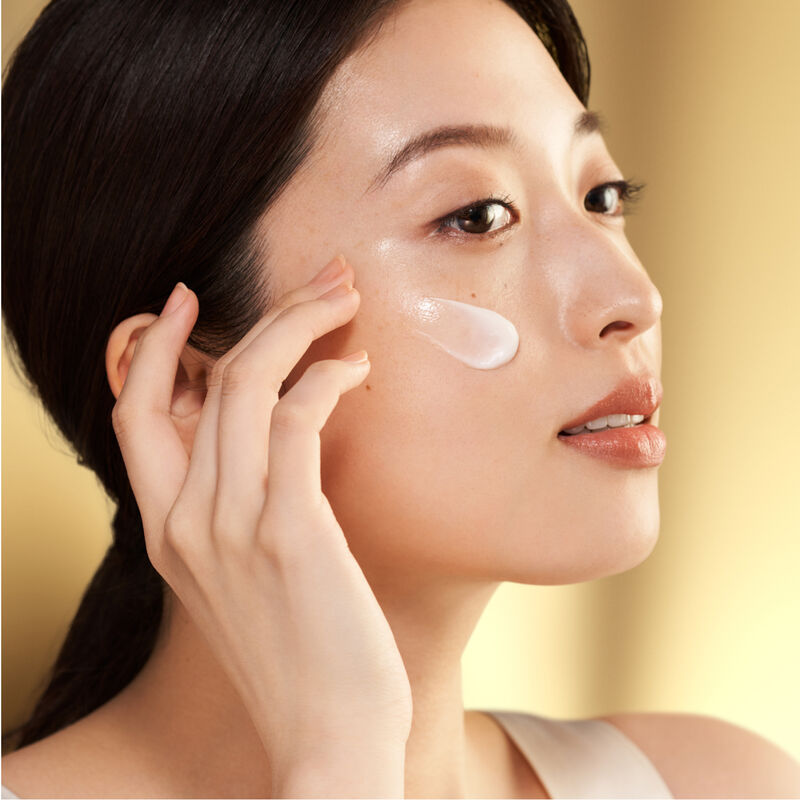 A  model gently applying the Shiseido Vital Perfection Uplifting and Firming Advanced Cream to her upper right cheekbone.  